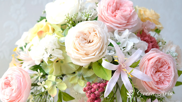 白く丸いばらとピンクのばら落ち着いたイエローのばらのプリザーブドフラワーアレンジメント。６枚の花弁の造花のネリネがエレガント。お花のアップの写真。